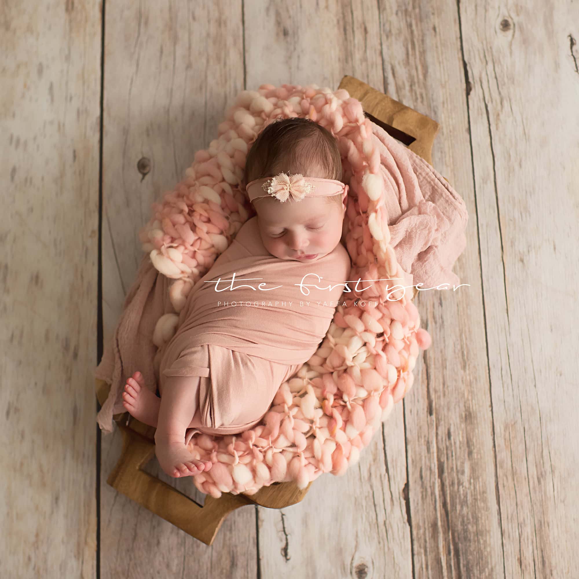 Newborn baby girl sleeping on a cozy blanket in a wooden cradle.