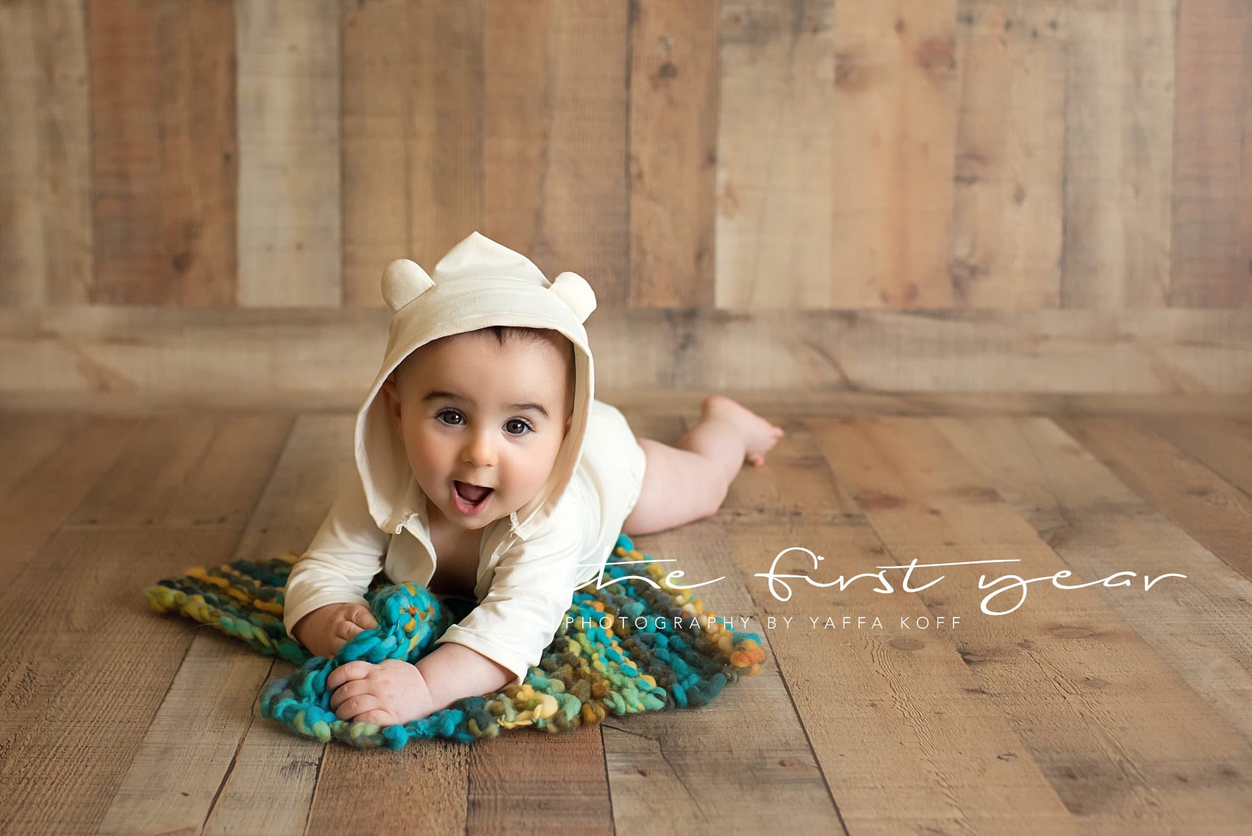 Baby lying on a colorful blanket during milestone photoshoot.