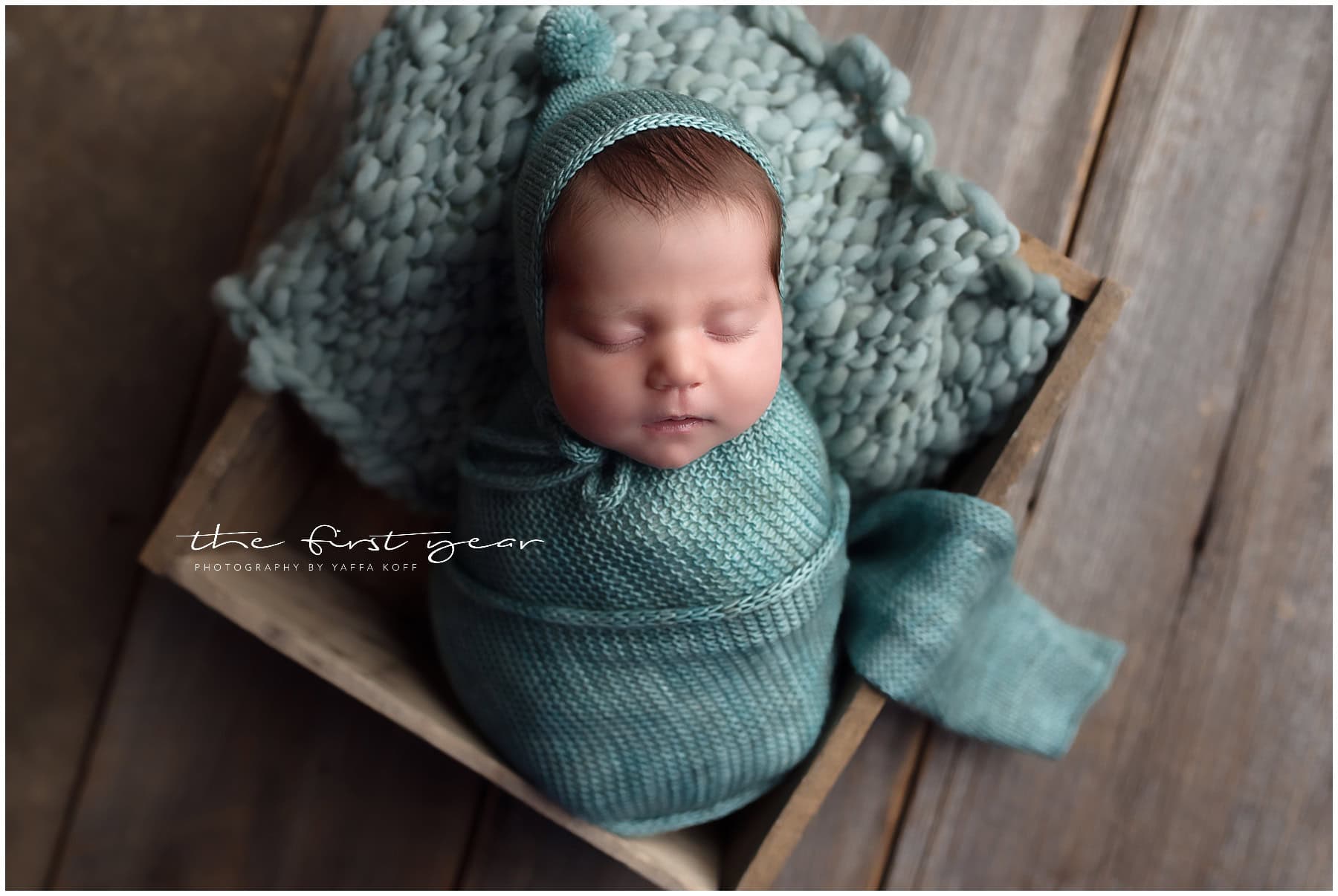 Adorable newborn baby wrapped in a blue swaddle with a matching hat, sleeping peacefully on a wooden.