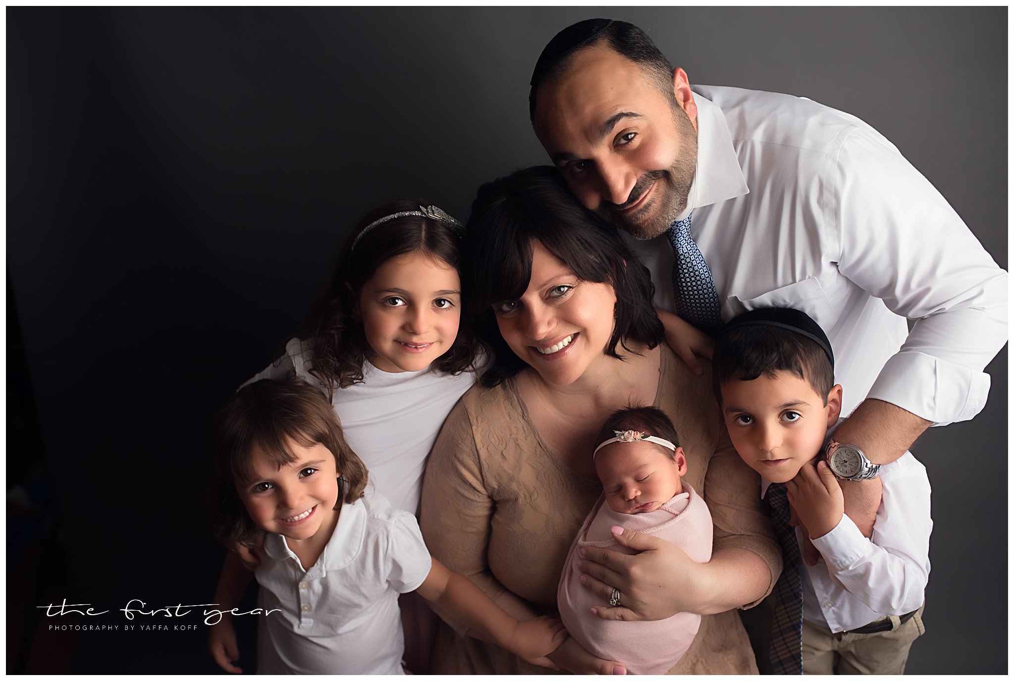 Family with newborn girl in a professional studio setting, smiling warmly.