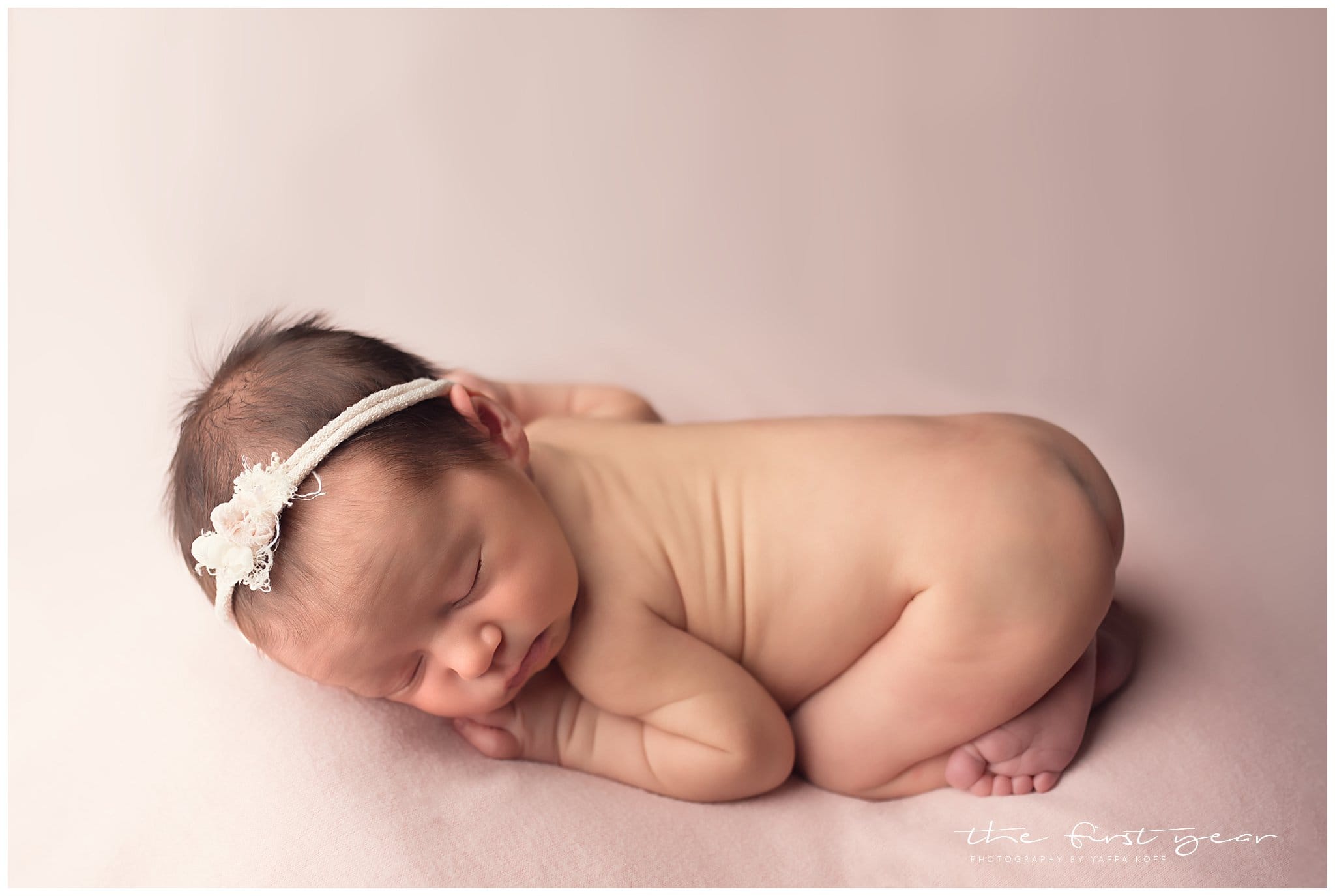 Newborn baby girl sleeping peacefully with a floral headband.