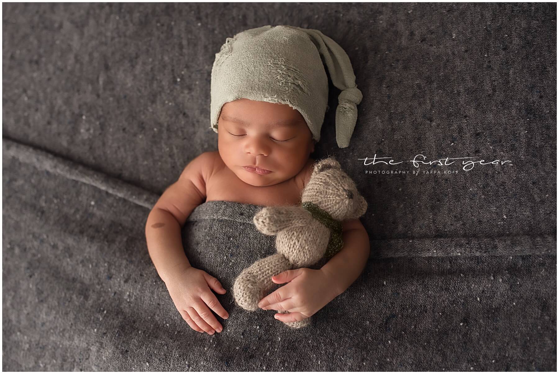 Adorable newborn baby sleeping with a stuffed animal on a soft gray blanket.