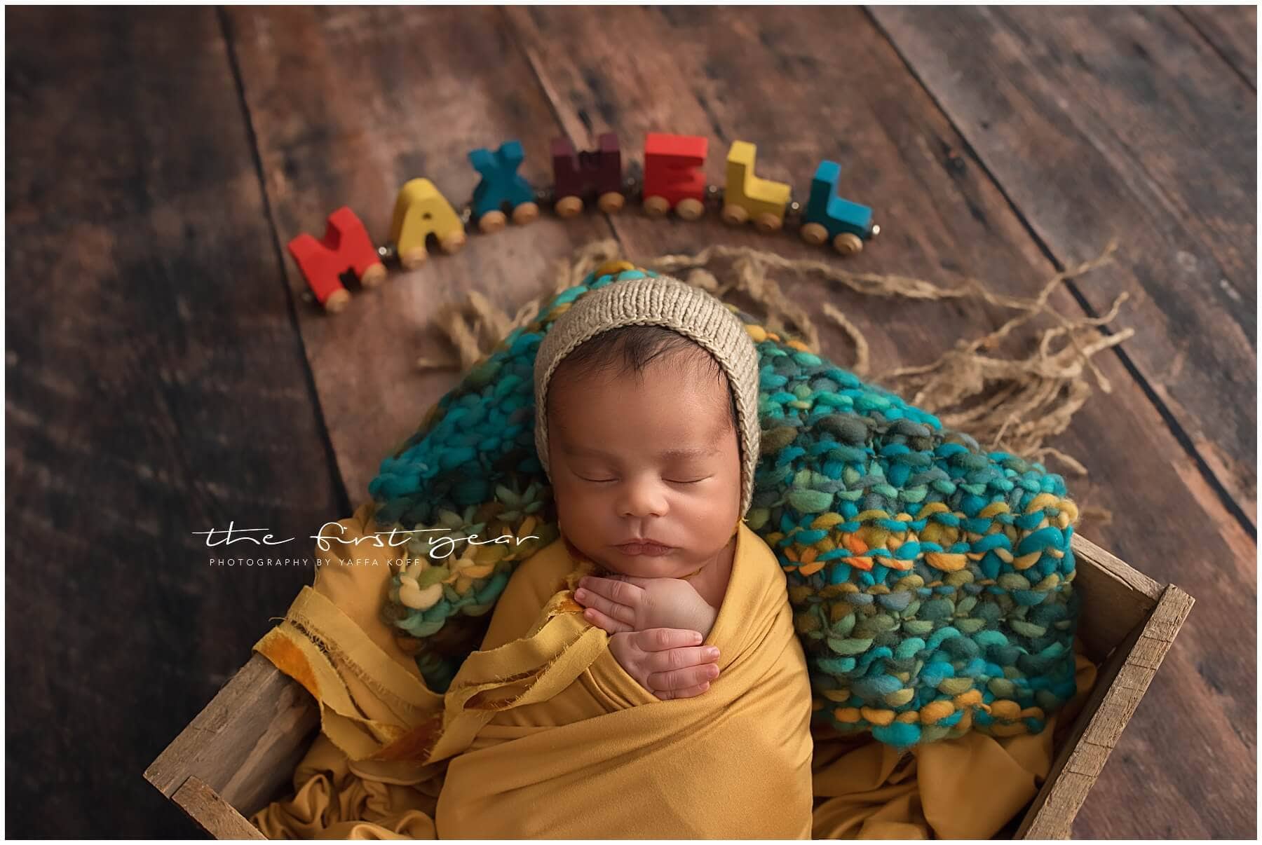 Newborn baby sleeping with colorful "Maxwell" blocks in a rustic wooden box.