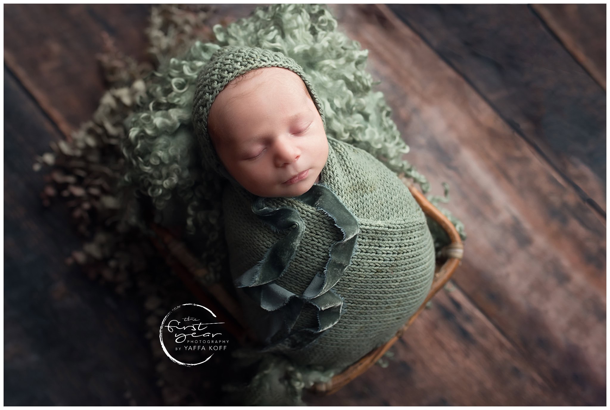 Newborn baby Rami sleeping peacefully wrapped in green knit, cozy in a basket with rustic wooden bac.