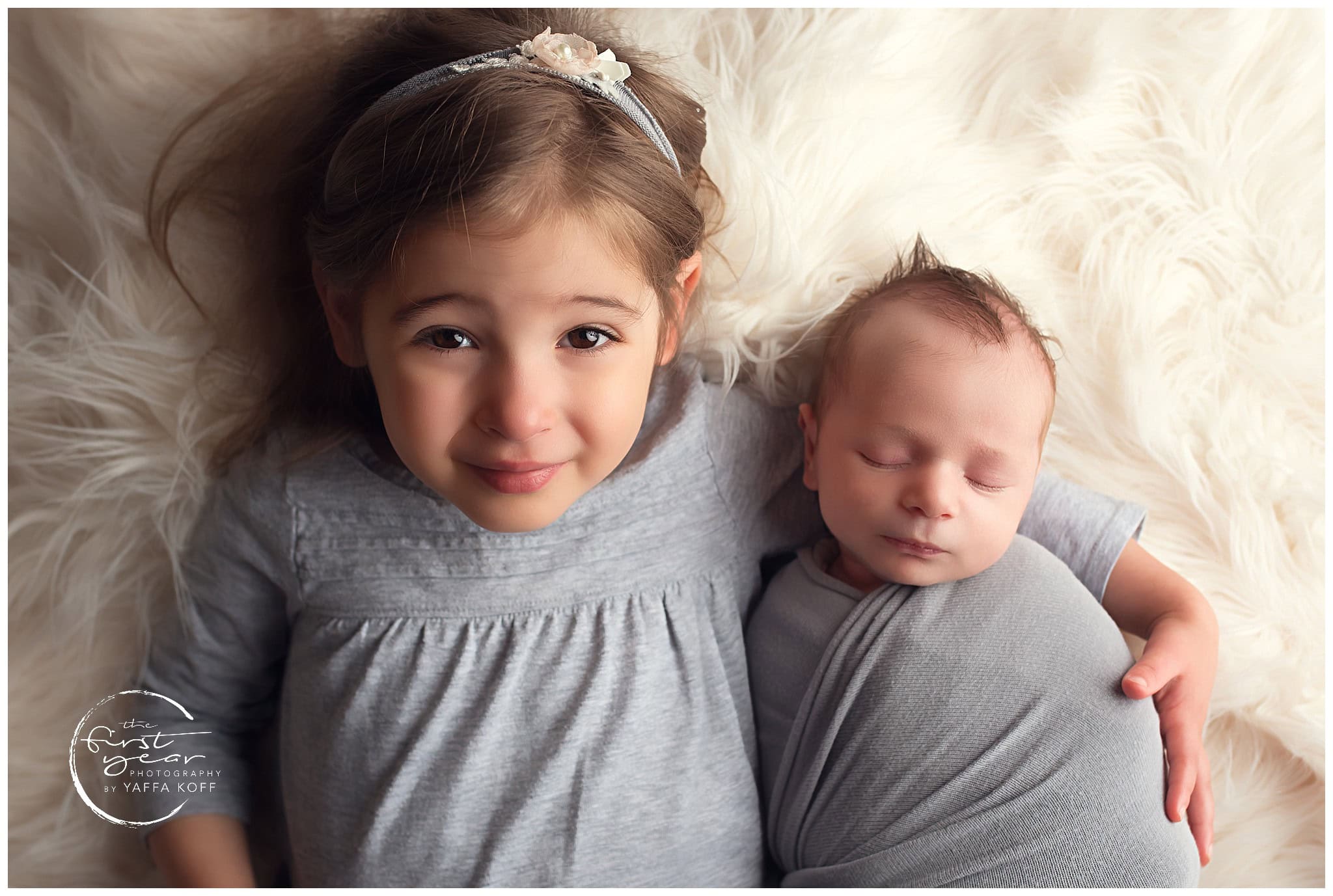 Baby Rami and older sister lying together on a soft, fluffy blanket.