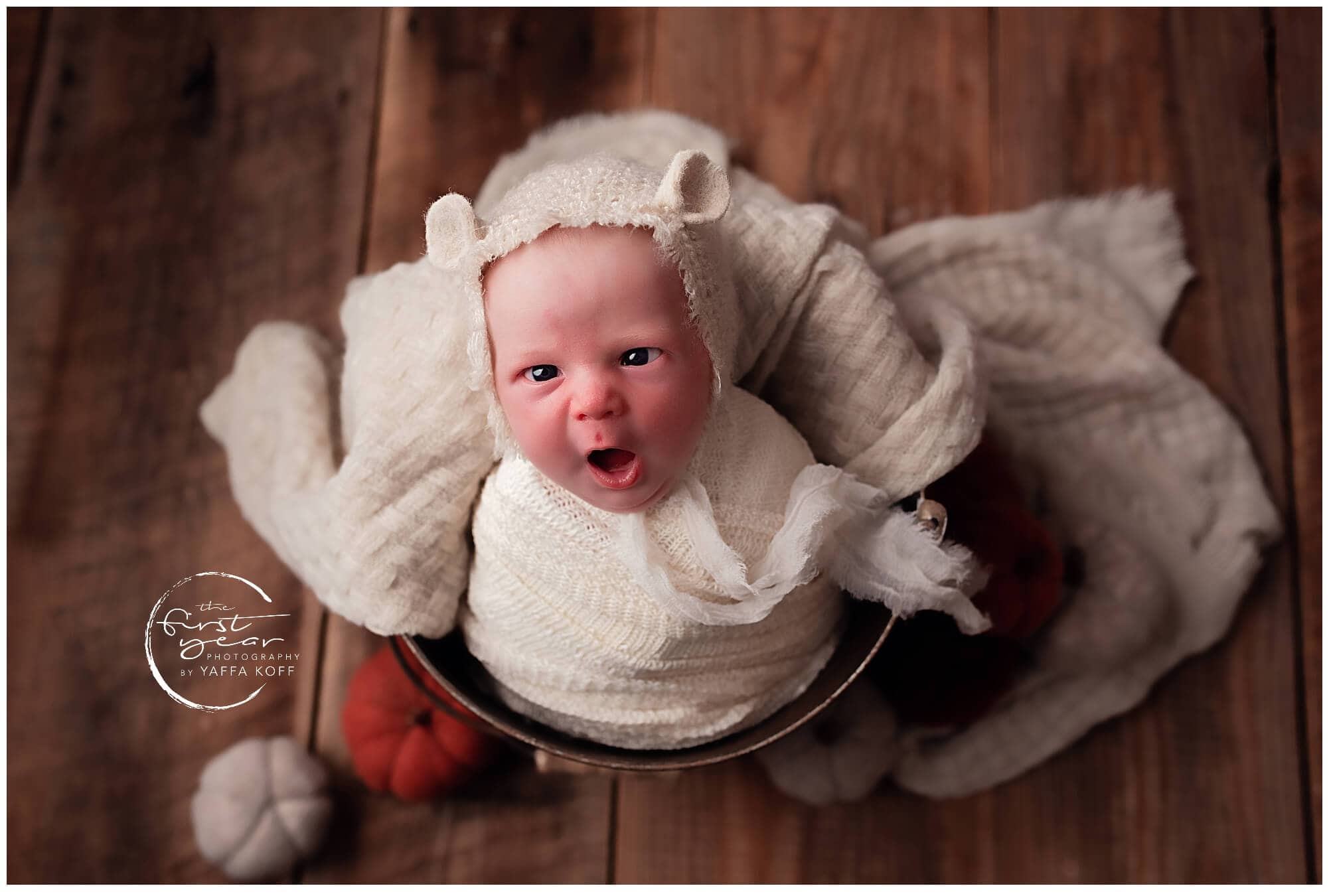 Adorable newborn baby Yehuda dressed in a cute bear hat, sitting on a wooden floor.