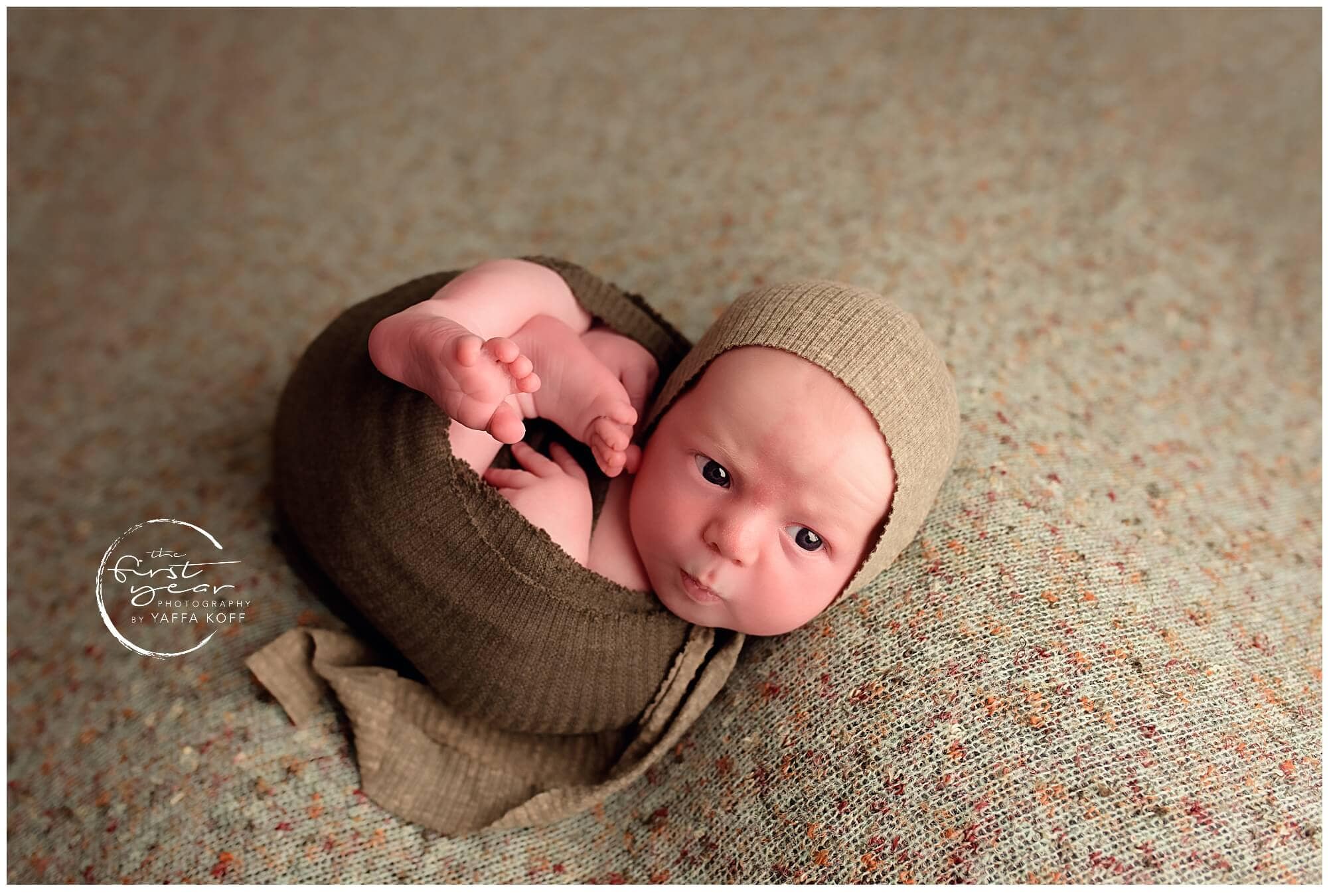 Adorable newborn baby Yehuda lying on a textured blanket, wrapped in a cozy brown outfit with a beig.