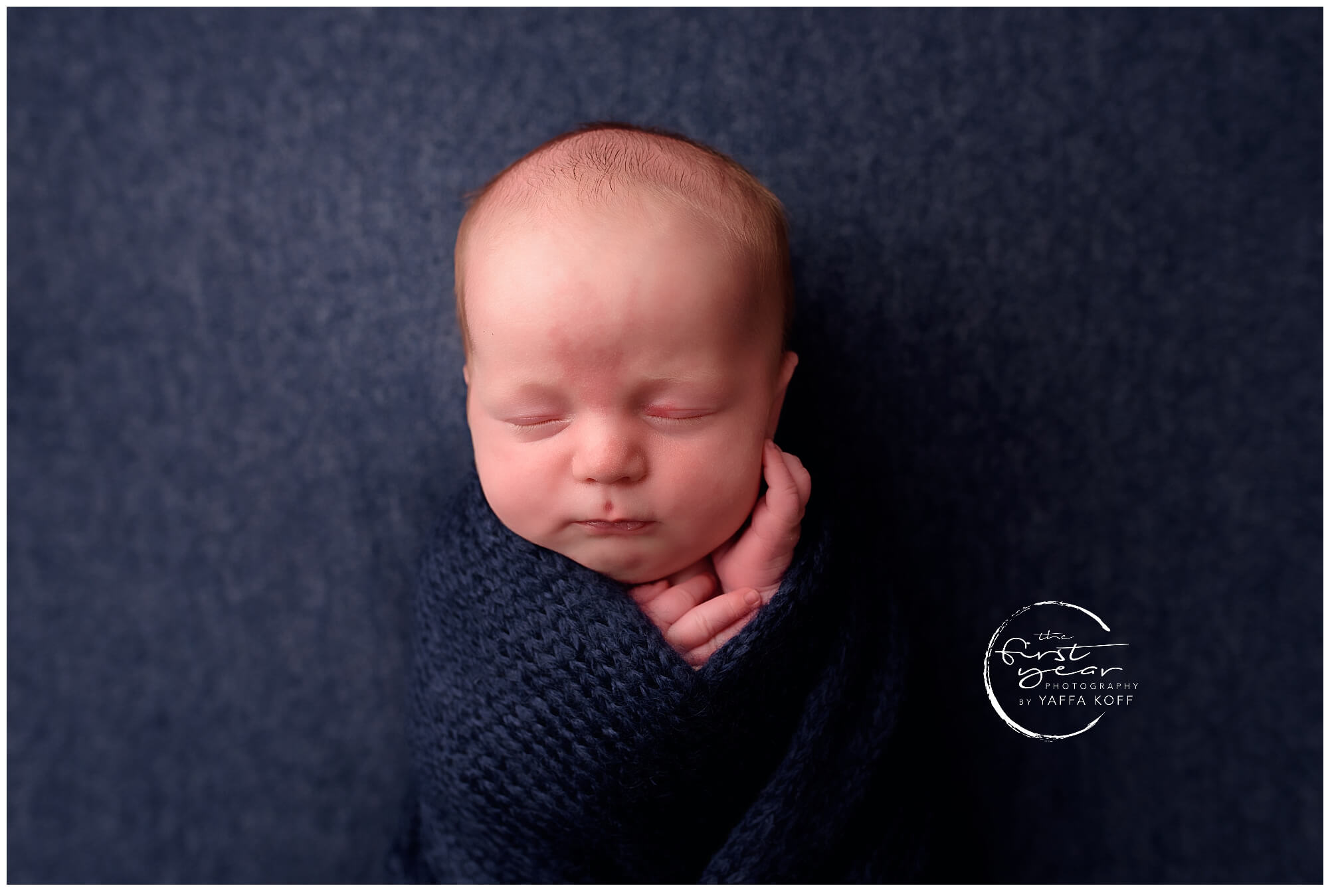 Adorable newborn baby Yehuda wrapped in a navy blanket, sleeping peacefully.
