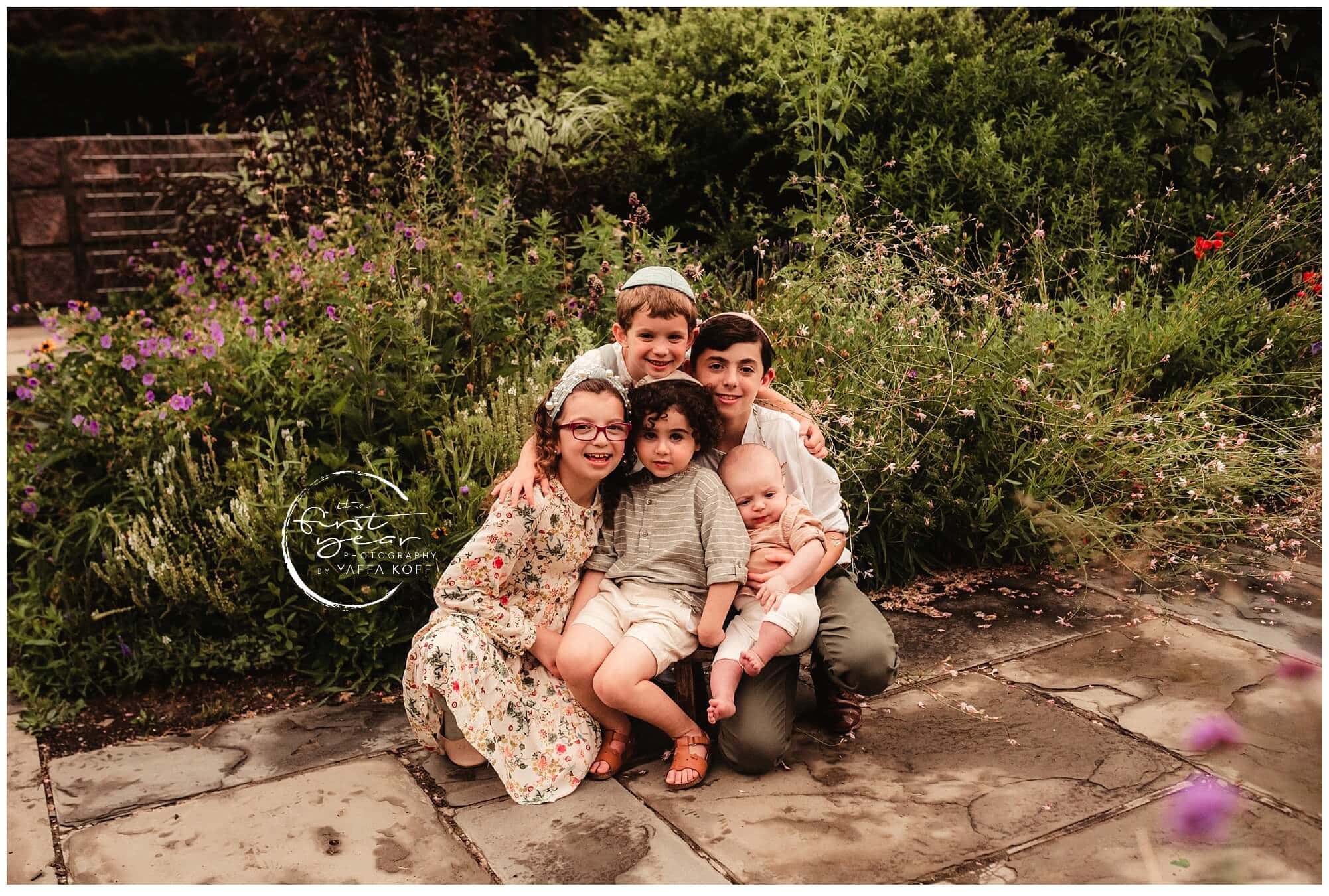 Family outdoor portrait in a garden setting, capturing a joyful moment with children and parents.