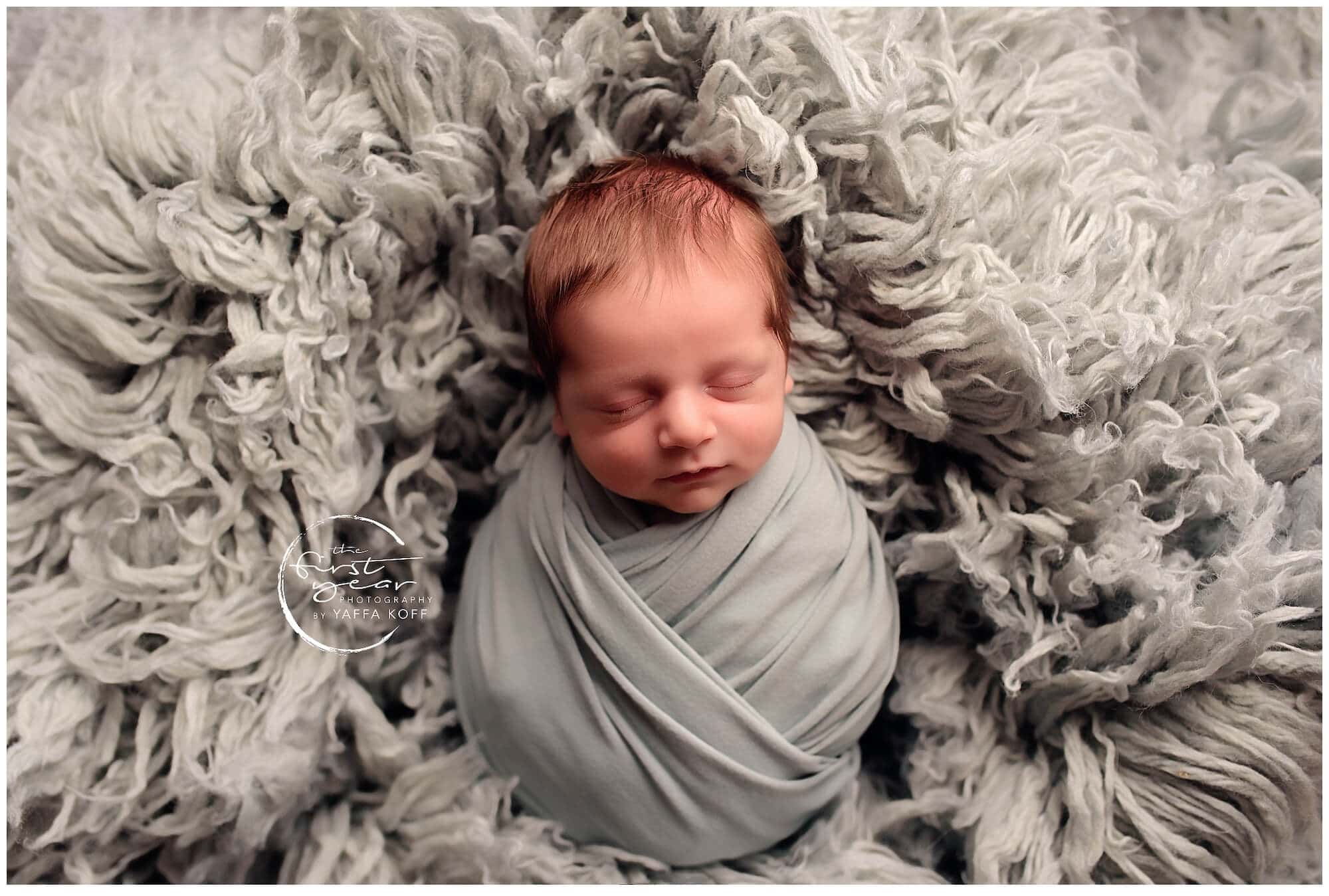 Adorable newborn baby Nathan peacefully sleeping wrapped in a soft gray blanket.
