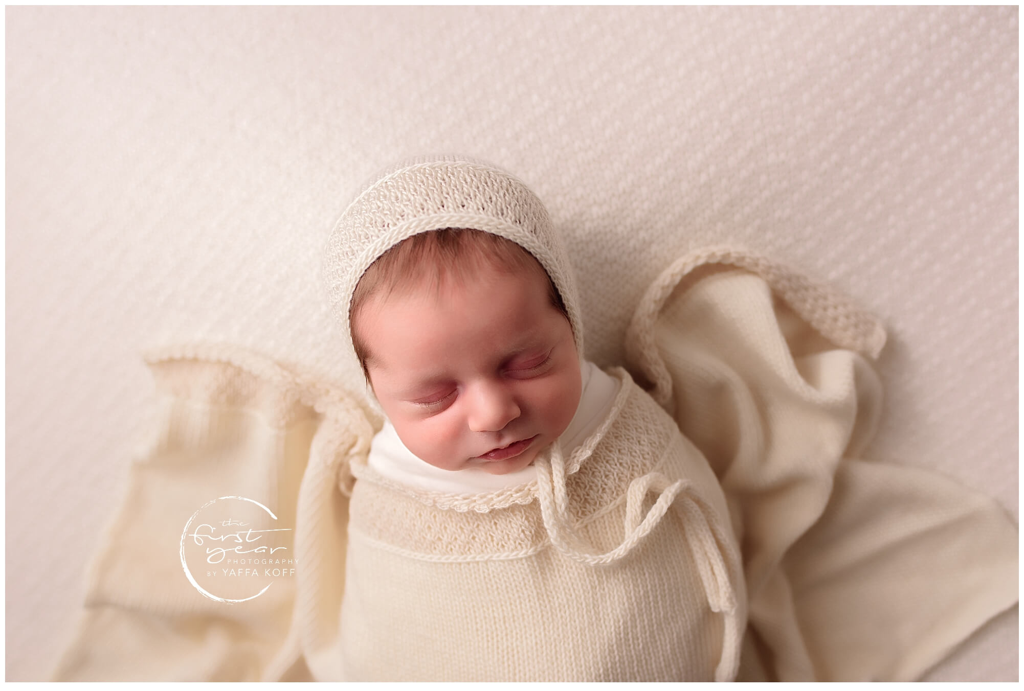 Newborn baby Nathan sleeping peacefully in a cozy cream outfit.