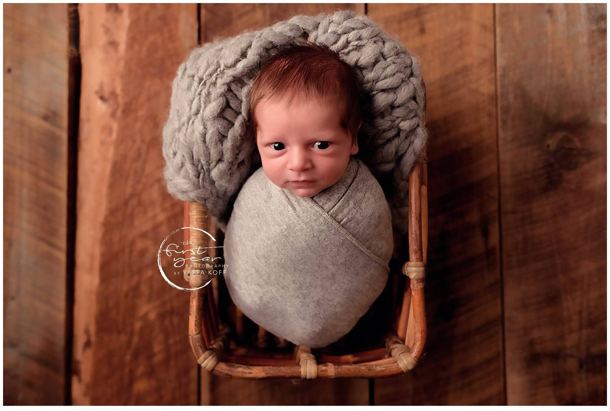 Adorable newborn baby wrapped in gray blanket in a wooden cradle.