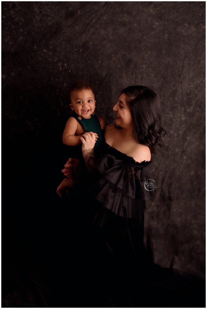Happy toddler with a big smile holding a woman during cake smash session.