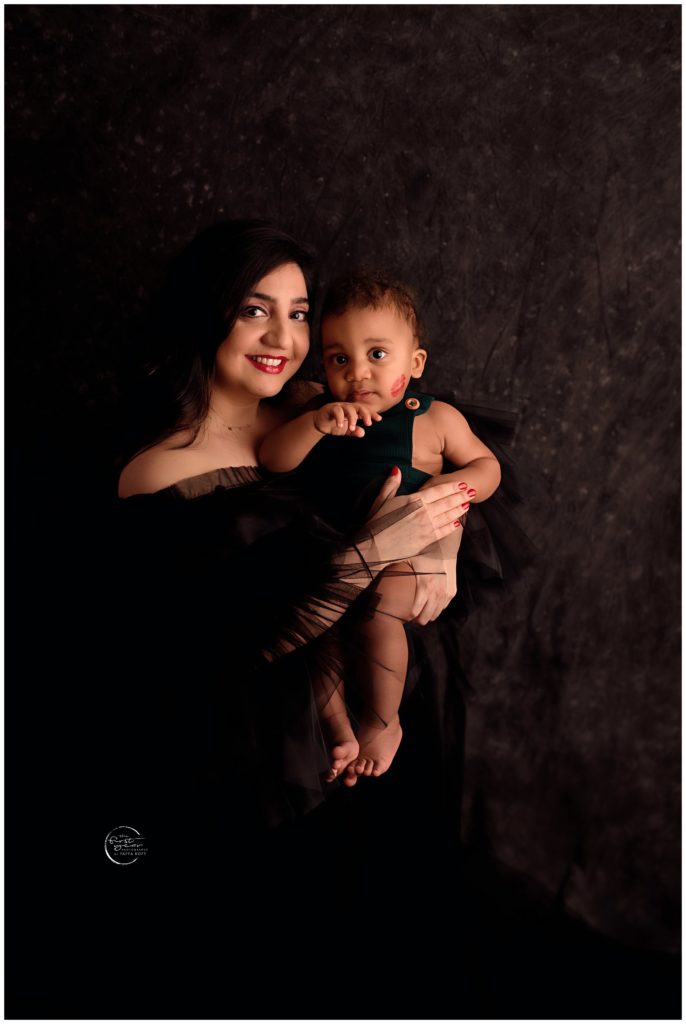 Mother holding her smiling baby girl in a studio setting.
