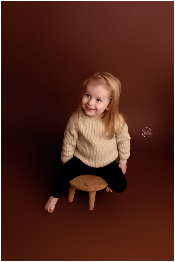 Child sitting on a small wooden stool with a joyful expression.