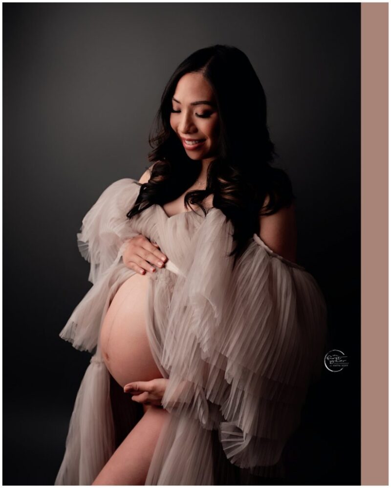 Pregnant woman in a flowing, elegant dress, showcasing her baby bump during a maternity session.