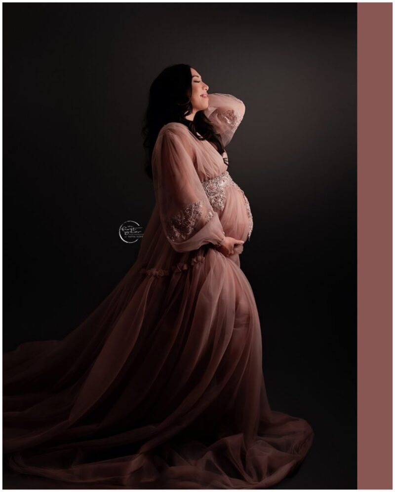 Beautiful pregnant woman in a flowing pink maternity gown, posing gracefully.