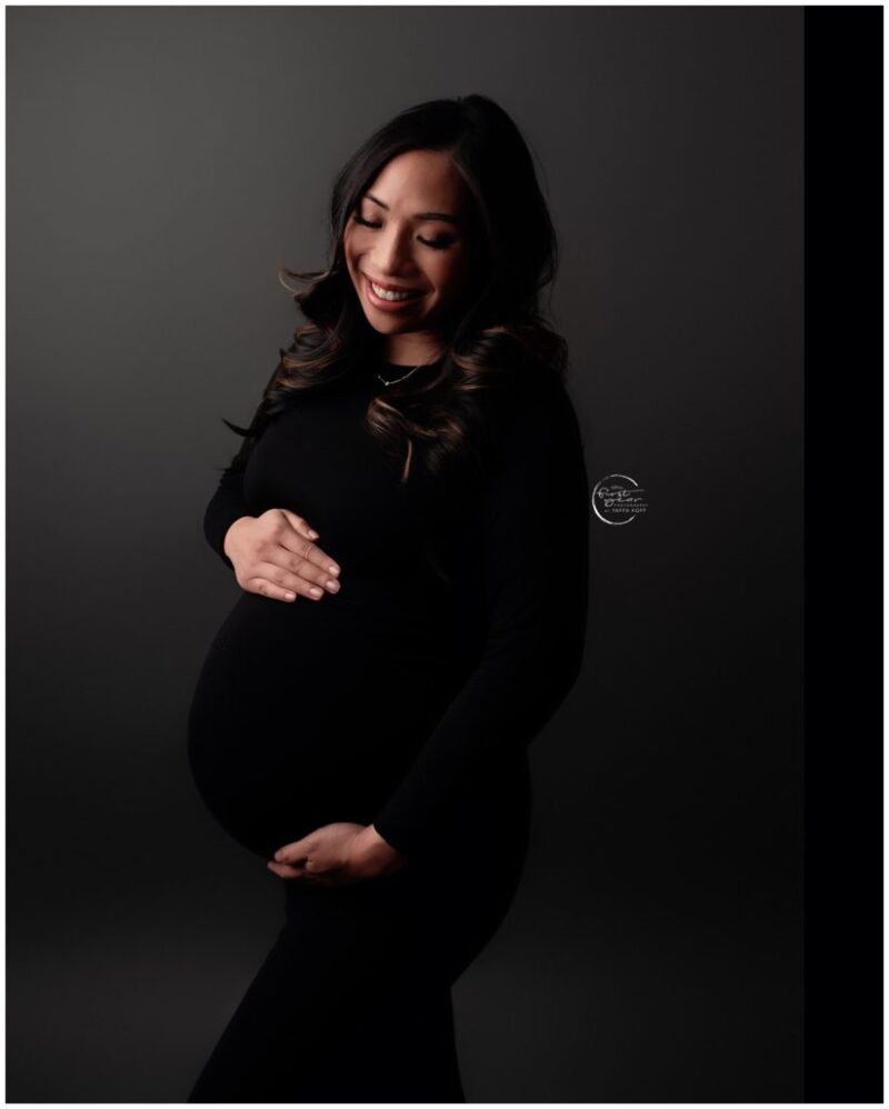 Pregnant woman smiling and holding her belly during a maternity photoshoot.