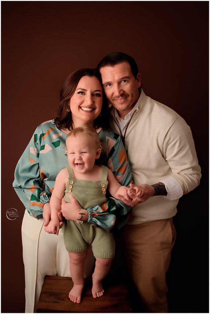 Happy family celebrating birthday with a cake smash, smiling and holding their toddler.