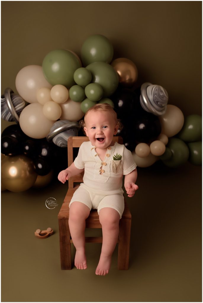 Baby smiling during birthday cake smash with balloons backdrop.