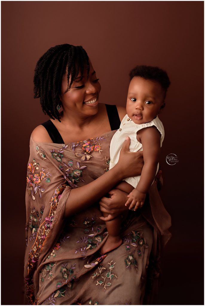 Mother holding her baby girl, both smiling, in a warm studio setting.