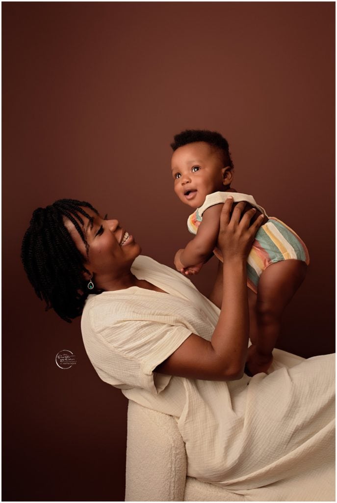 Happy baby held by smiling mom in a cozy studio setting.