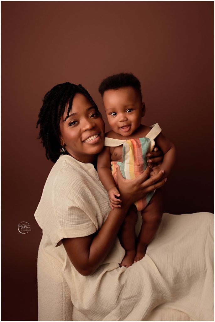 Mother holding her smiling baby girl in a studio setting.
