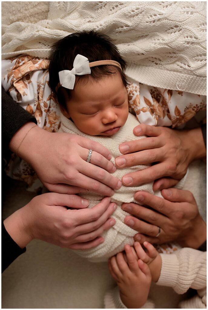 Newborn baby girl with family hands, cozy and peaceful.