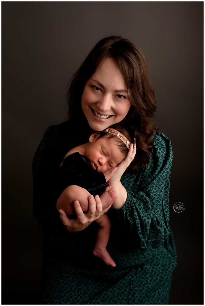 Smiling mother holding her sleeping newborn girl during a portrait session.