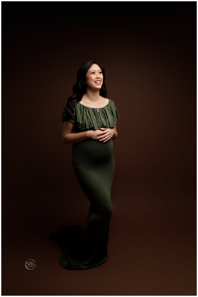 Beautiful pregnant woman in a dark studio, wearing a green dress, smiling softly.