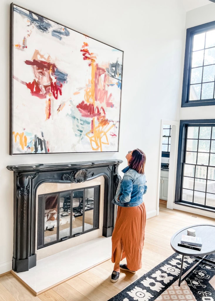 Interior of a stylish living room with a woman admiring artwork above the fireplace.
